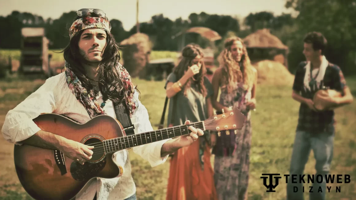 A man dressed in 60's fashion hippie style plays an acoustic guitar outdoors, wearing a colorful headscarf, sunglasses, and layered accessories, with friends in similar attire in the background at a field.