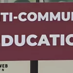 A maroon sign with bold white letters displaying the words "Anti-Communist Education," symbolizing a focus on promoting anti-communist perspectives in educational settings.