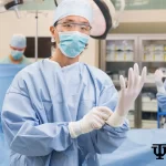 Surgeon wearing gloves in a health theater with medical staff in the background, preparing for surgery. Concept Health Theater Throup.