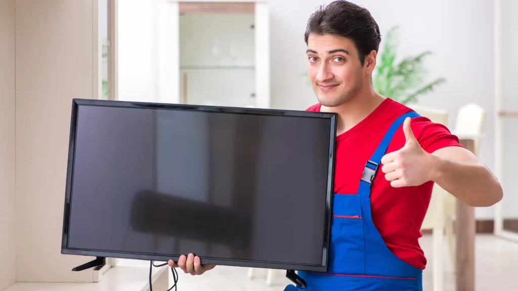 Smiling technician holding a flat-screen TV, ready for installation of the Lumi TV Professional Android Signage system.