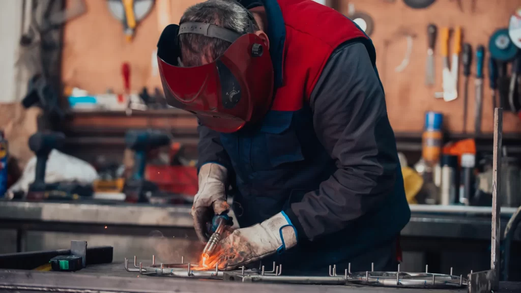 A welder working on metal fabrication in an industrial workshop, illustrating heavy-duty manufacturing related to where Powermatic tools are manufactured.