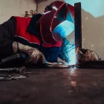 A welder in protective gear producing sparks during welding, emphasizing craftsmanship and manufacturing processes linked to where Powermatic tools are manufactured.