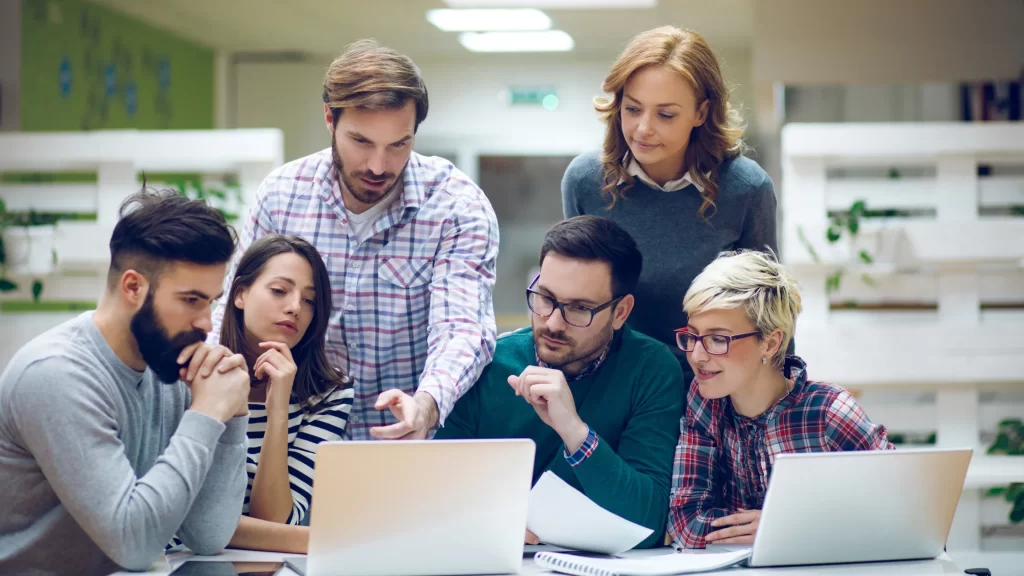 A diverse team of professionals collaborating on a laptop, focusing on Co-Development Software and problem-solving.